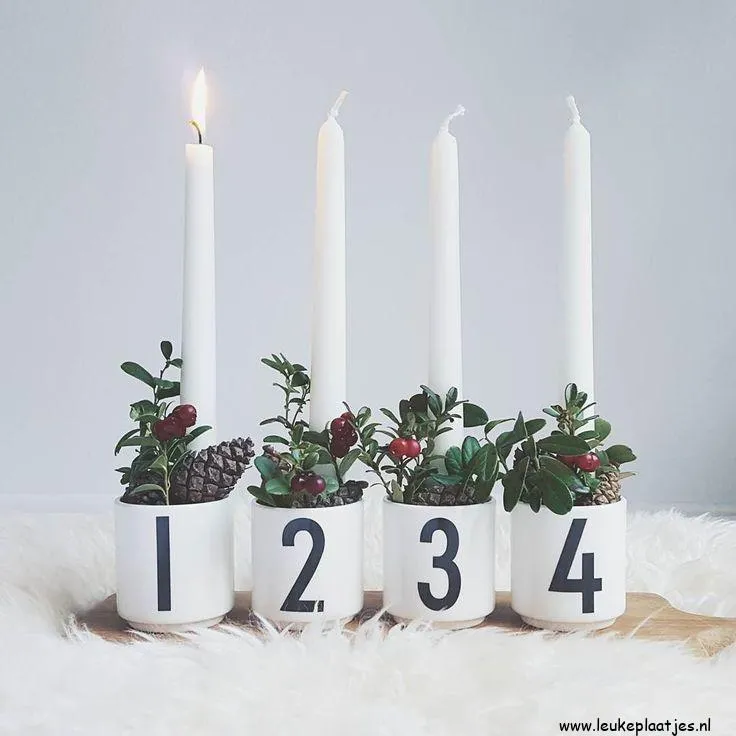 Vier witte kaarsen in nummers met groen en rode bessen in decoratieve houders.