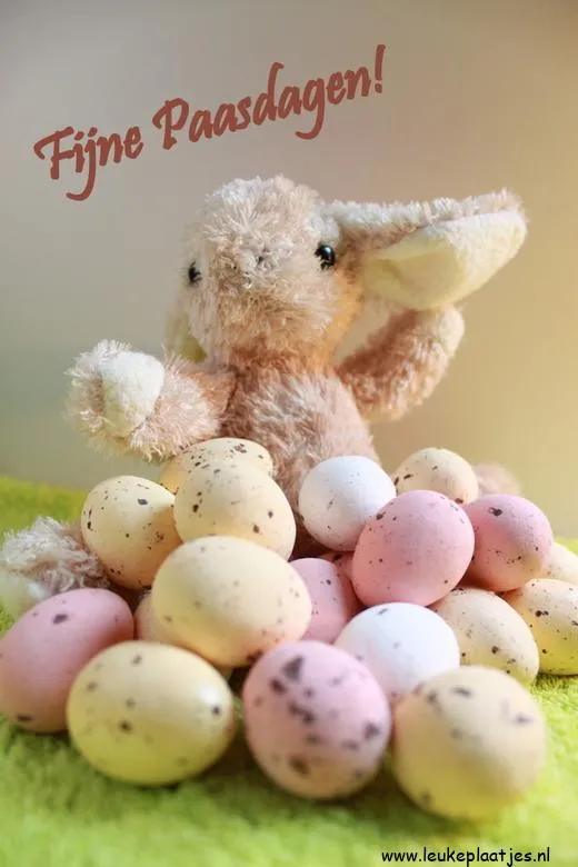 Pluche konijn met kleurige paaseieren op een groene ondergrond.